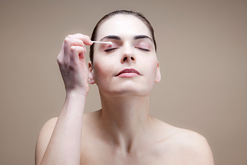 A serene young woman using a cotton swab on her eye